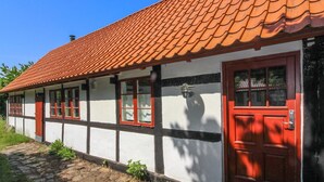 Un edificio tradicional con techo de tejas rojas, paredes blancas con detalles negros y ventanas de marcos rojos.