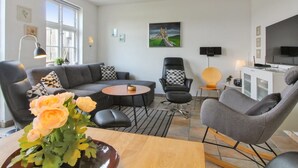 A modern living room with a grey sofa, a round coffee table, and a TV. There are two chairs, a small table with a lamp, and a painting on the wall. - "Karoline" - 6km from the sea by Interhome (Aakirkeby)