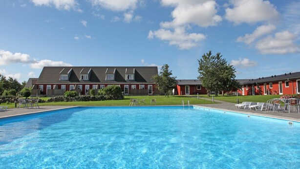 A swimming pool with a view of a row of red buildings in the background. - "Karoline" - 6km from the sea by Interhome (Aakirkeby)