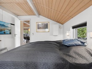 A bedroom with a large bed, a framed picture on the wall, and a window with a view of trees.