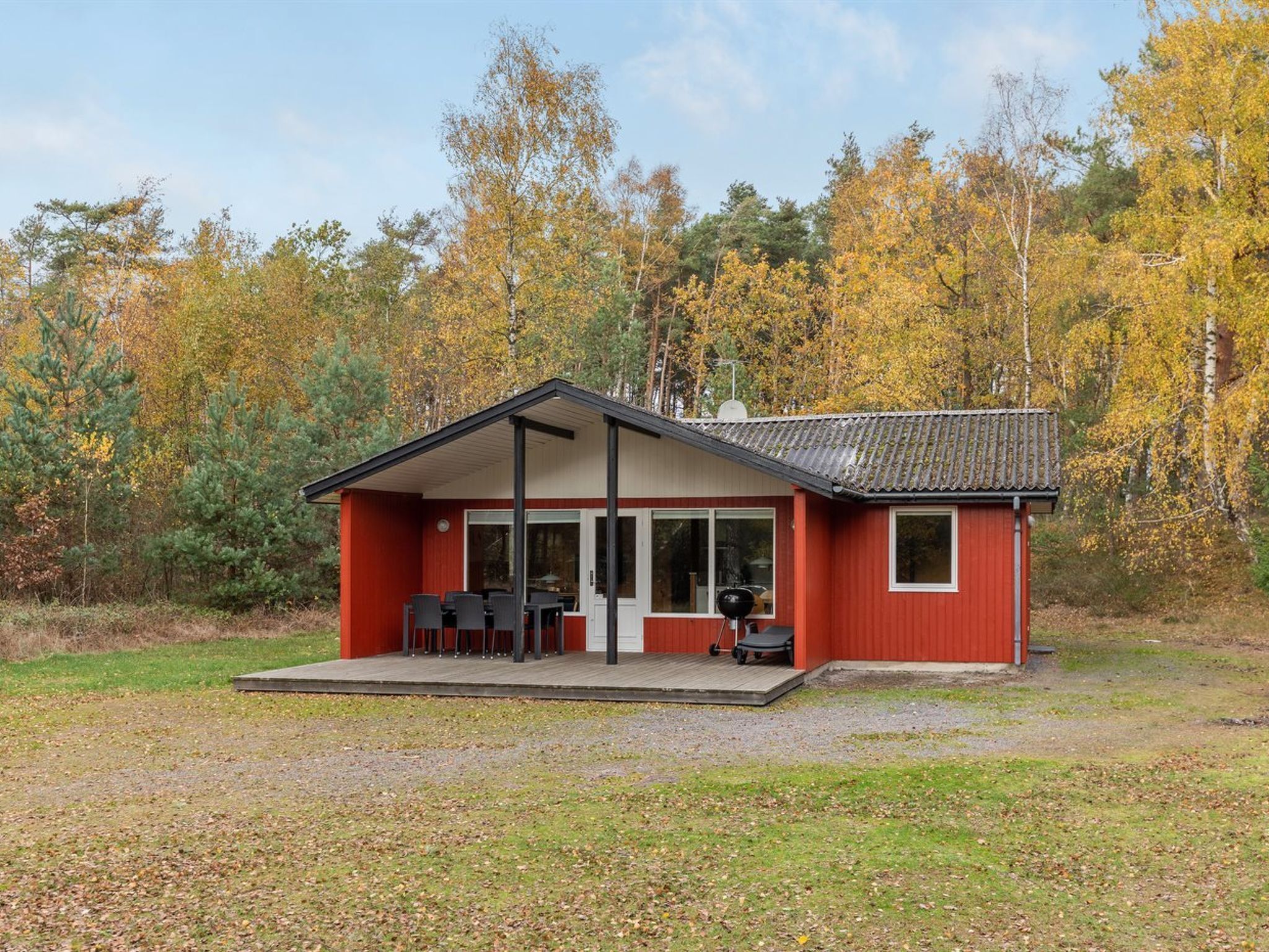 A red cabin with a covered patio and a dining area, surrounded by autumn foliage.