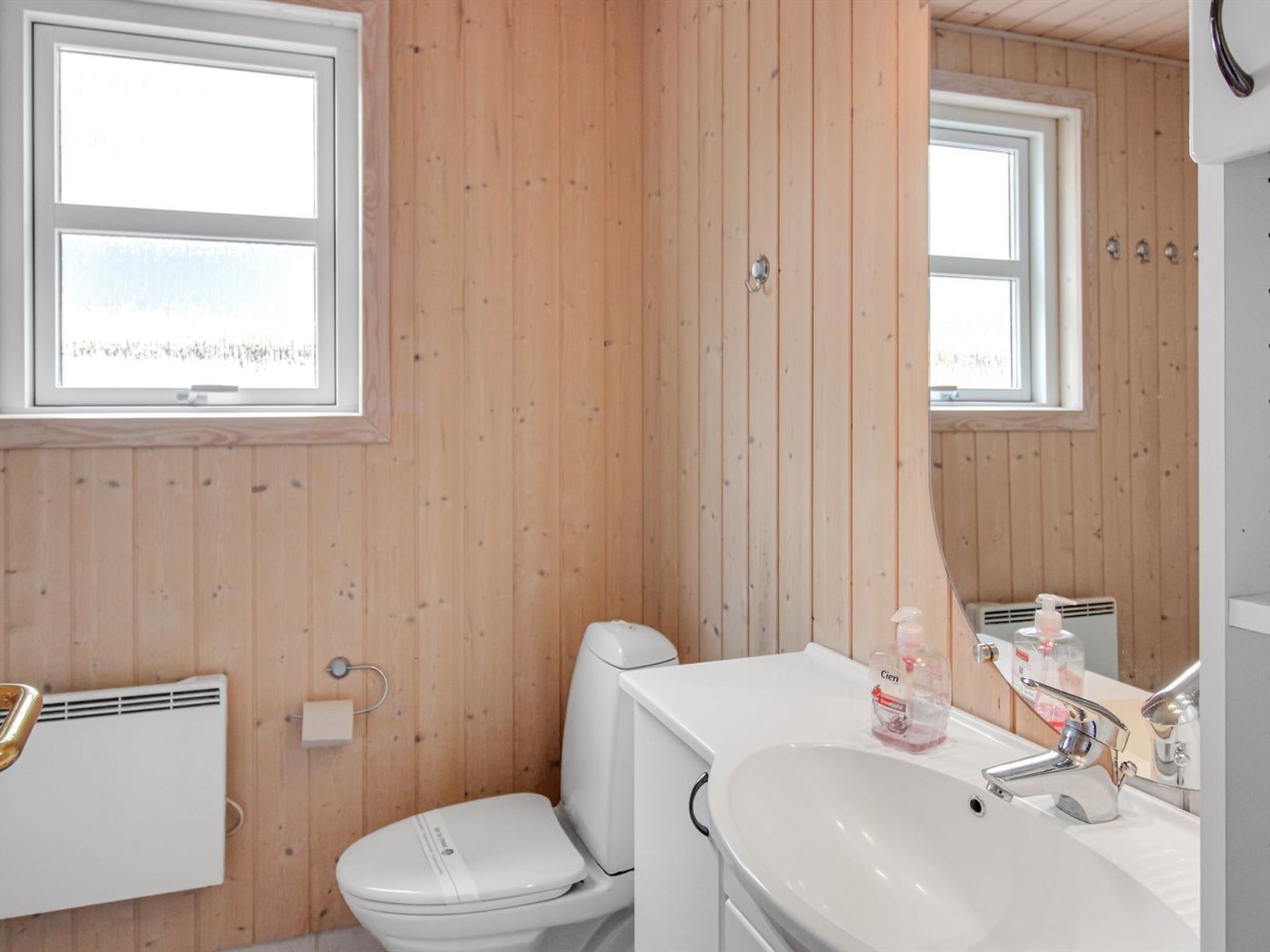Ett badrum med träpanel på väggarna, en vit toalett, ett vitt handfat och en spegel.