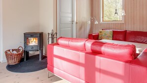 Una habitación acogedora con un sofá de cuero rojo, un estufa de leña, una cesta de mimbre y una ventana con vistas a árboles.