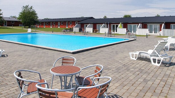 A swimming pool with lounge chairs and tables, surrounded by a building with a red facade and a covered patio area. - "Thorke" - 5km from the sea by Interhome (Aakirkeby)