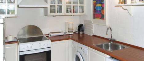 A compact kitchen with white cabinetry, a built-in oven, a washing machine, and a coffee maker.