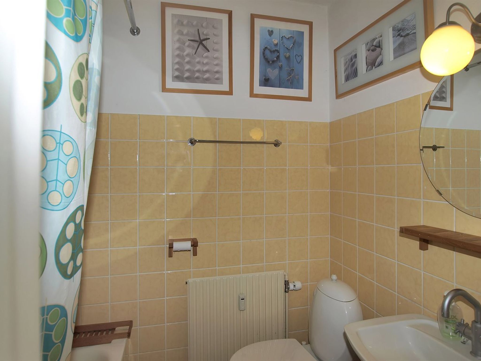 Een badkamer met beige tegels, een toilet, een wastafel, een handdoekhouder en ingelijste foto's aan de muur.