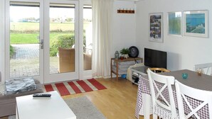 A modern living room with a TV, dining table, and chairs. There is a sliding glass door leading to a patio with a view of a green field. - "Thorke" - 5km from the sea by Interhome (Aakirkeby)
