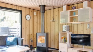 Ein gemütliches Wohnzimmer mit Kaminofen, einer Couch, einem Esstisch und einer TV-Konsole.