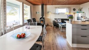 A cozy living area with a wooden ceiling, a fireplace, a dining table with fruit, a sofa, and a kitchen area. - "Bondi" - 150m from the sea by Interhome (Aakirkeby)