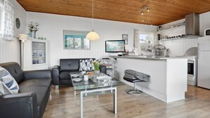 A modern living space with a wooden ceiling, a black leather sofa, a glass coffee table, and a kitchen area with white cabinets and a built-in island. - "Bondi" - 150m from the sea by Interhome (Aakirkeby)