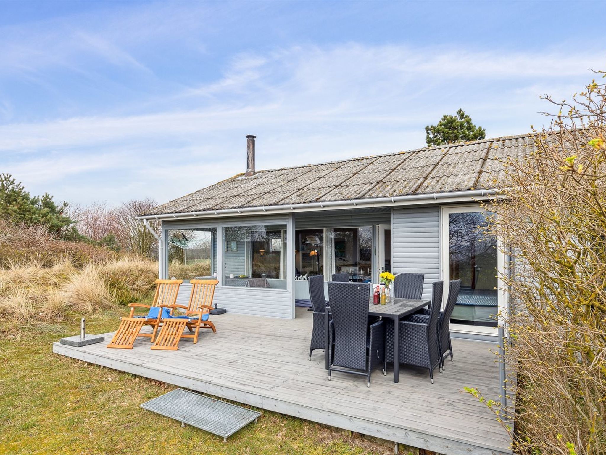 A modern house with a covered patio, outdoor seating, and a large window overlooking the landscape.