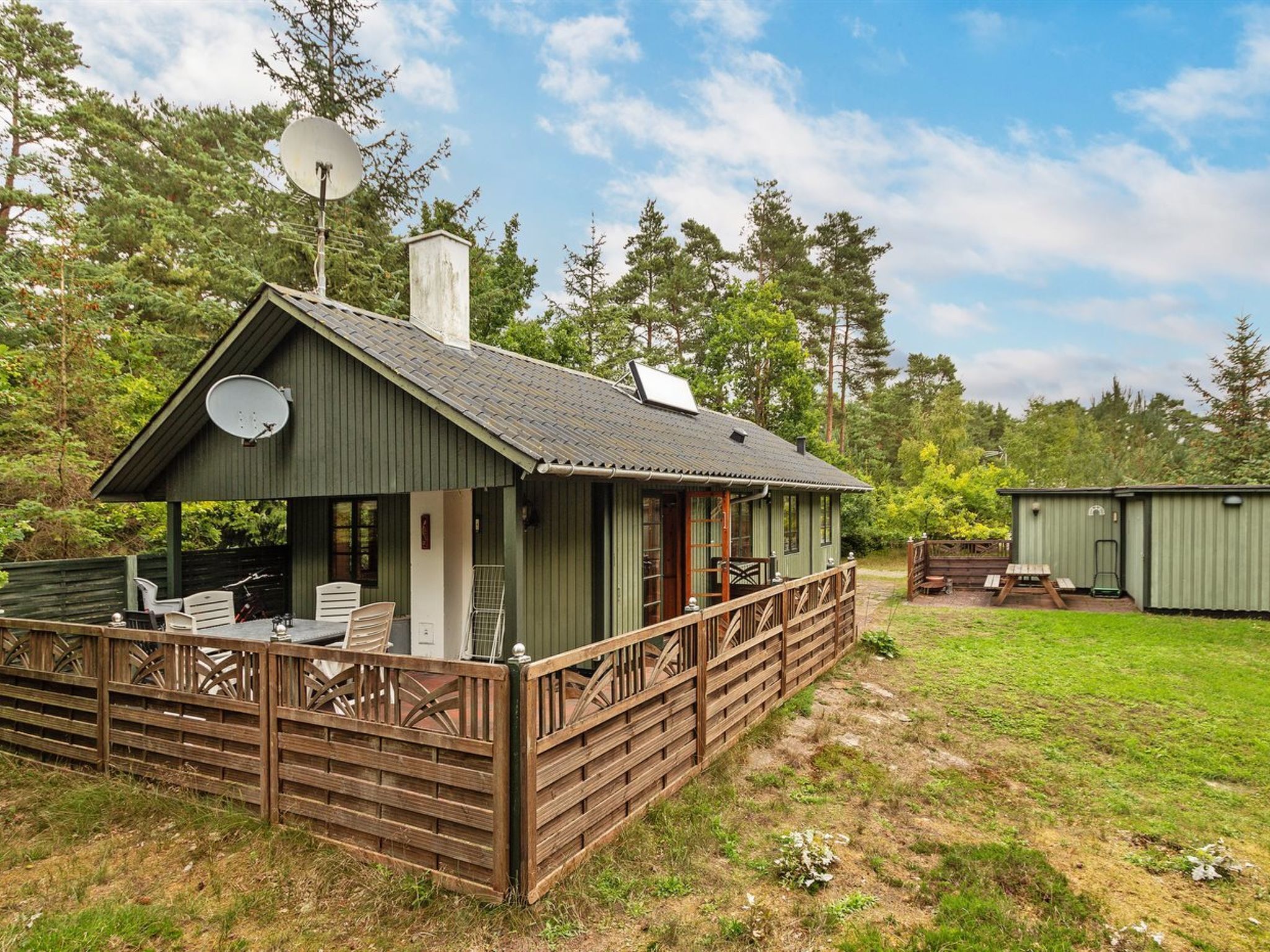 A small cabin with a porch, a satellite dish, and a wooden deck.