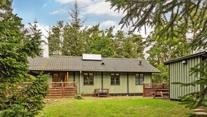 Un chalet rustique à l’extérieur vert, doté d’une terrasse en bois et d’une cour clôturée.