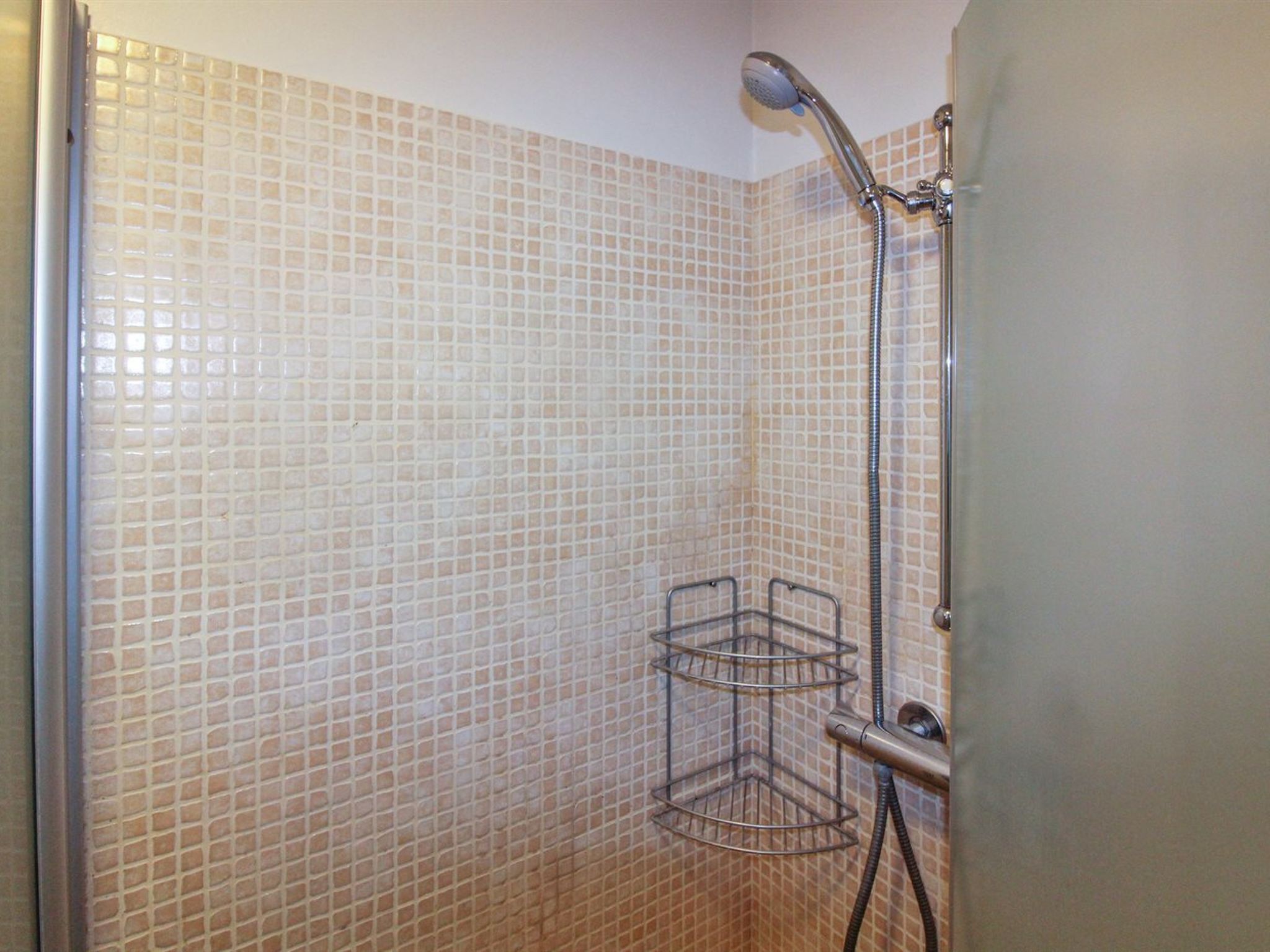 Een douche met een betegelde wand en een metalen douchekop.