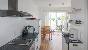 Eine moderne Küche mit schwarzem Arbeitsplatz, Edelstahlspüle und eingebautem Herd. Es gibt einen Essbereich mit Holztisch und Stühlen sowie einen Blick ins Freie durch eine Glastür.