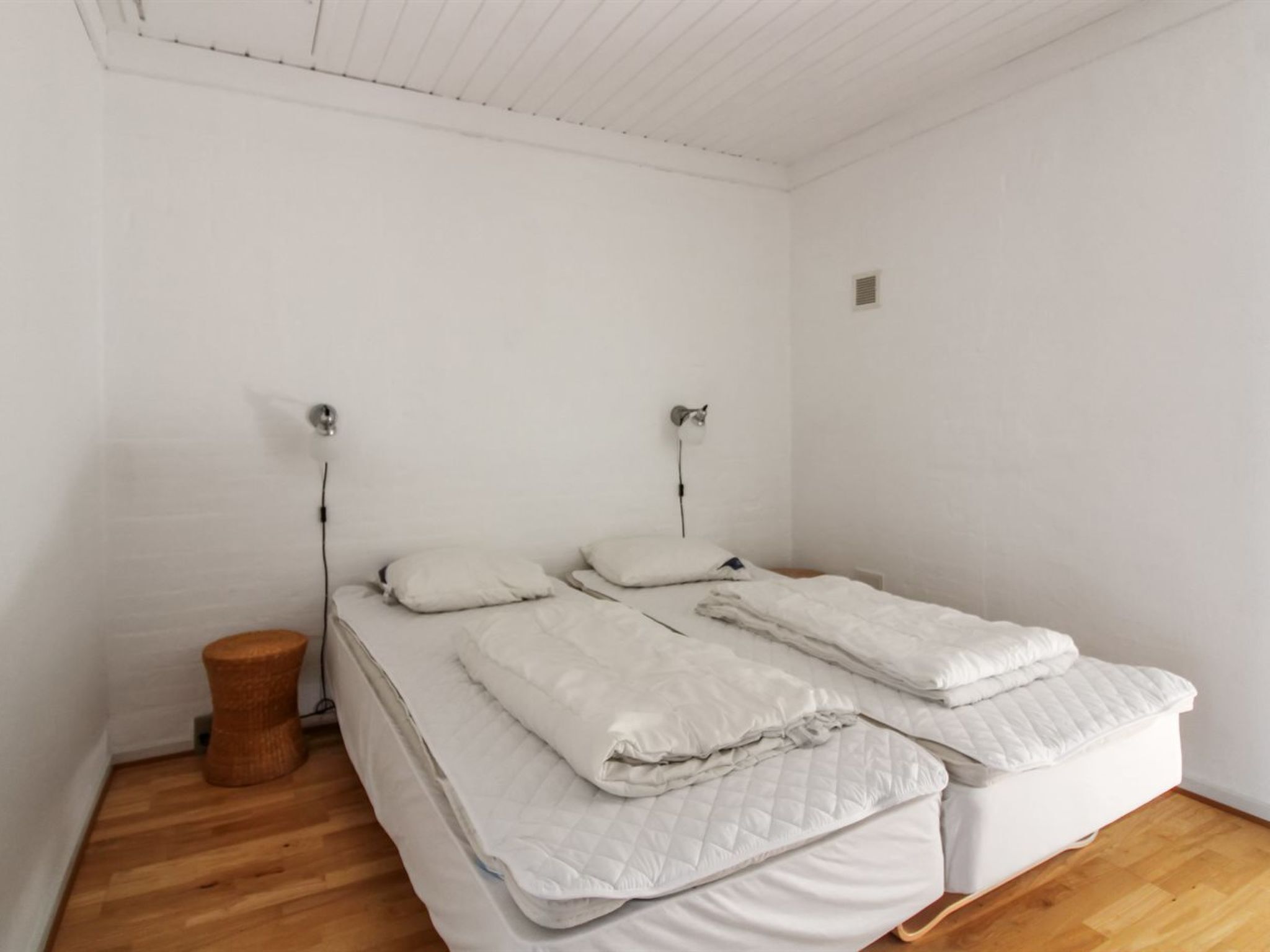 Une chambre à coucher minimaliste avec un lit simple, des murs blancs et un plancher en bois.