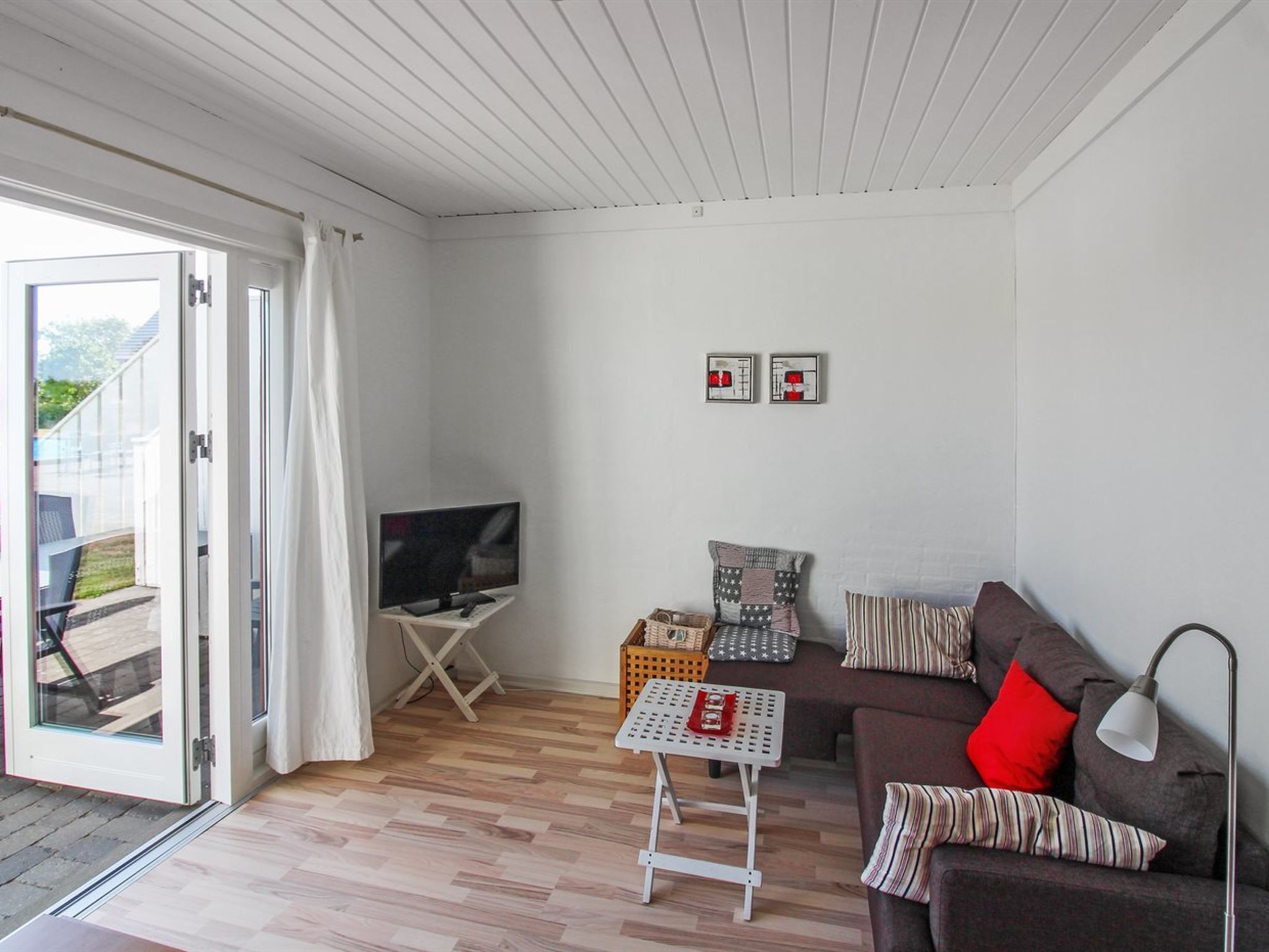 A living room with a TV, a sofa, a small table, and a window with curtains.