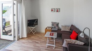 Ein Wohnzimmer mit Fernseher, einer Couch, einem kleinen Tisch und einem Fenster mit Vorhängen.