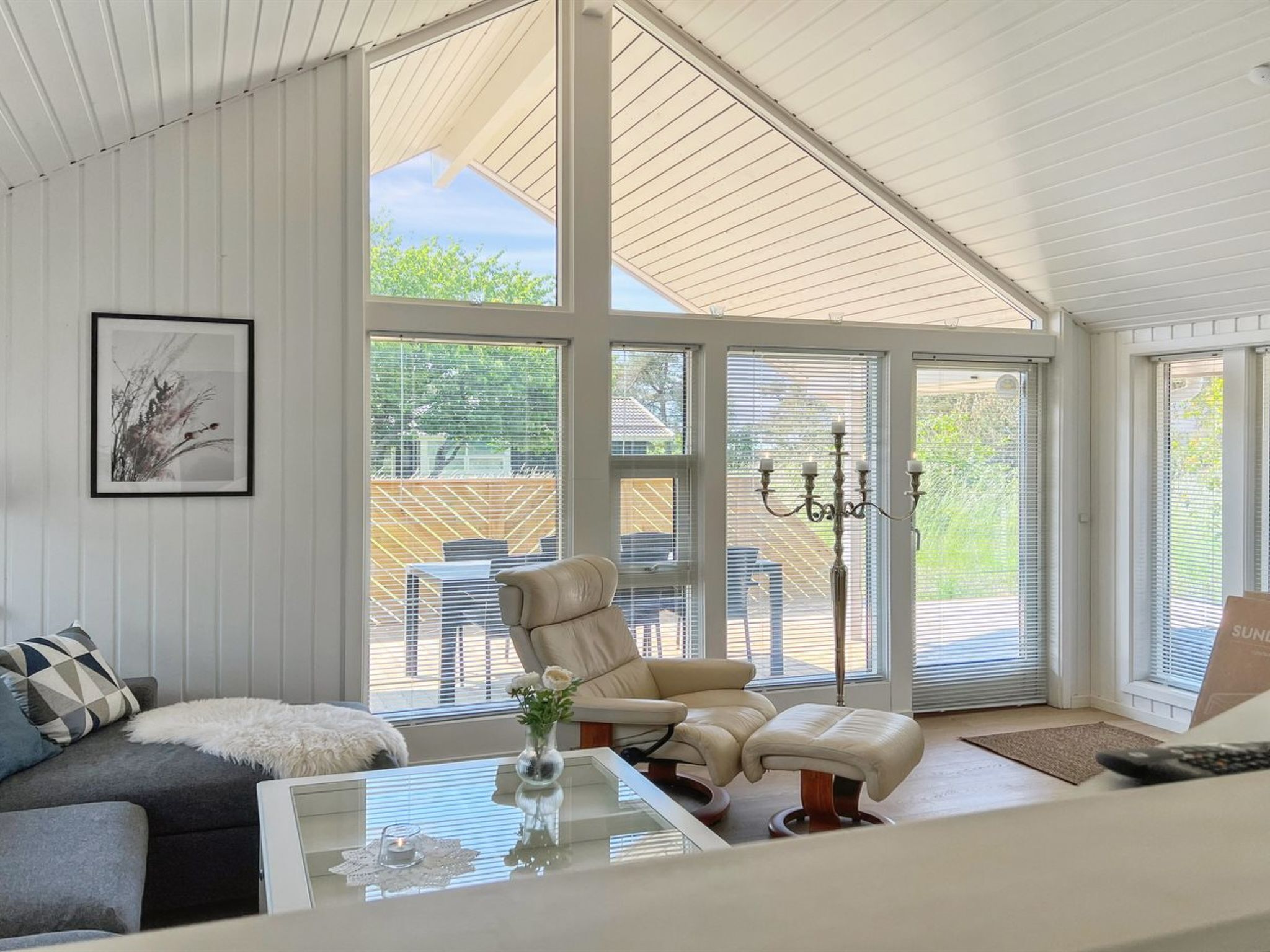 A spacious living room with a high ceiling, large windows, a comfortable sofa, a glass coffee table, and a chandelier.