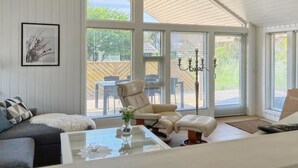 A spacious living room with a high ceiling, large windows, a comfortable sofa, a glass coffee table, and a chandelier.