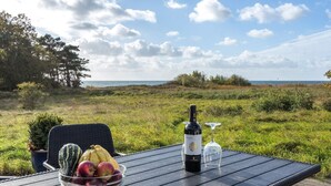 A table with a bottle of wine, a glass, and a bowl of fruit by a scenic view. - "Kajsa" - 50m from the sea by Interhome (Aakirkeby)