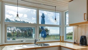 A kitchen with a large window, wooden cabinets, a sink, and a coffee maker. - "Kajsa" - 50m from the sea by Interhome (Aakirkeby)