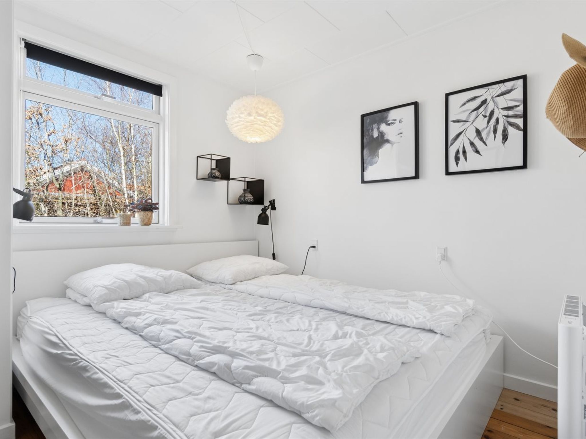 Un dormitorio con cama, ventana, lámpara colgante y cuadros en la pared.
