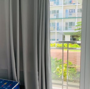 A room with a large window, curtains, and a view of a multi-story building with balconies.