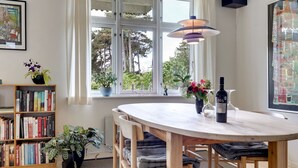 Ein Essbereich mit einem runden Tisch, Stühlen, einer Weinflasche und einem Bücherregal mit Büchern und Pflanzen.