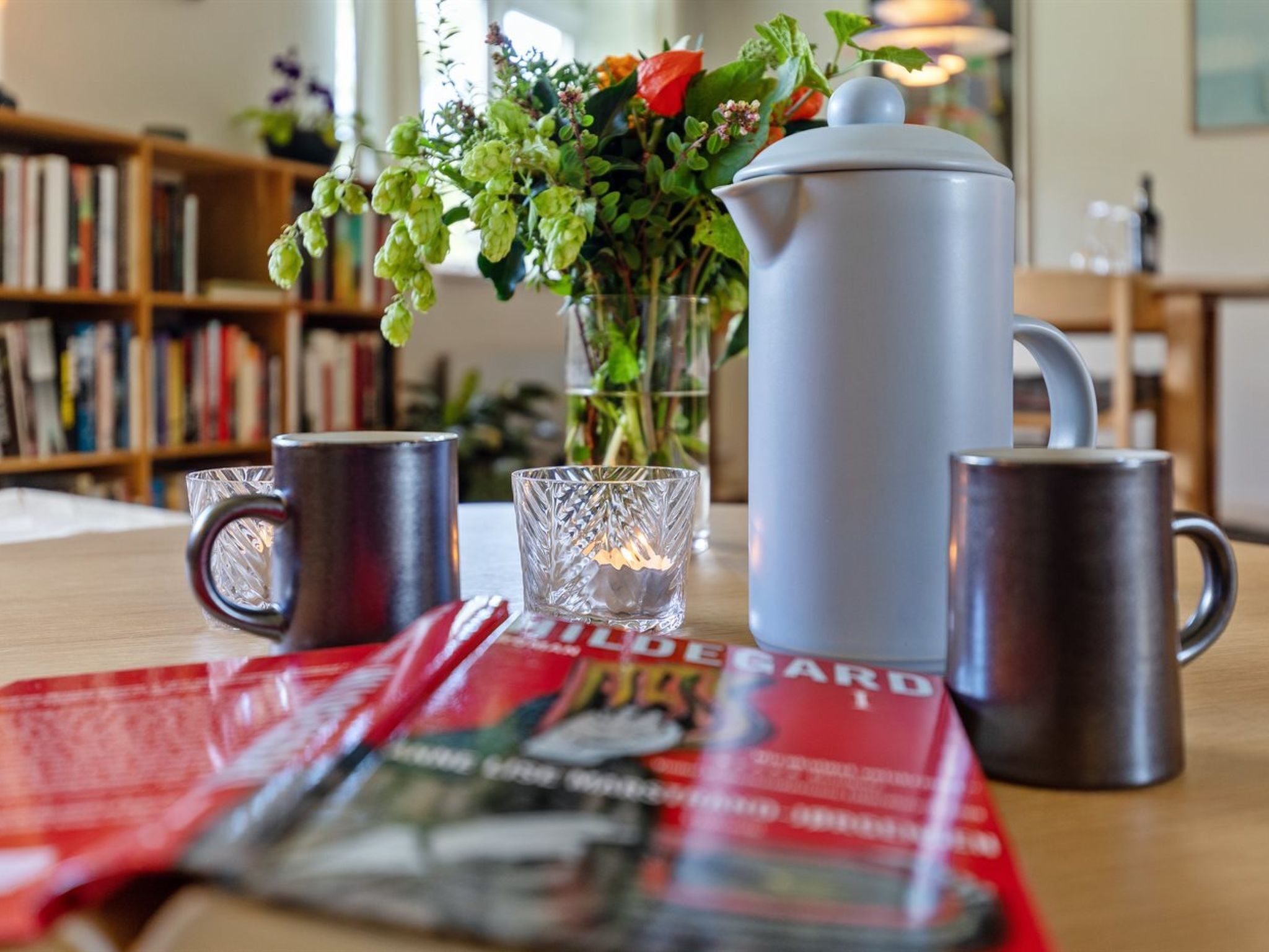 A table with a kettle, two mugs, a glass, and a magazine.