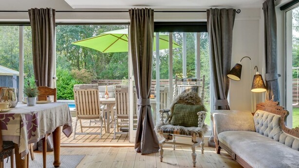 A cozy room with a sofa, dining table, and chairs. There is a large window with curtains and a view of the outdoors. - "Makrina" - 175m from the sea by Interhome (Jægerspris)