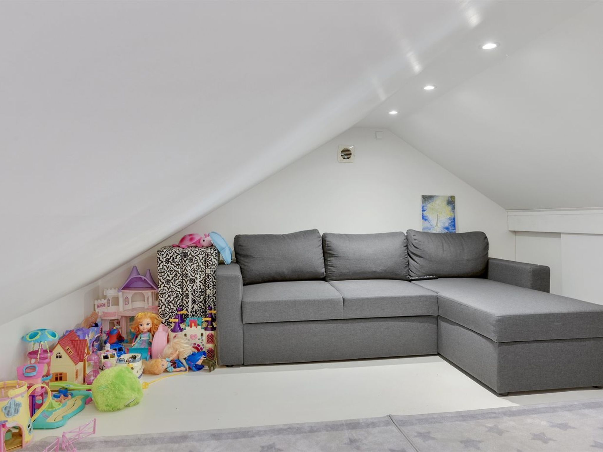 A modern, grey sectional sofa in a room with white walls and a sloped ceiling.