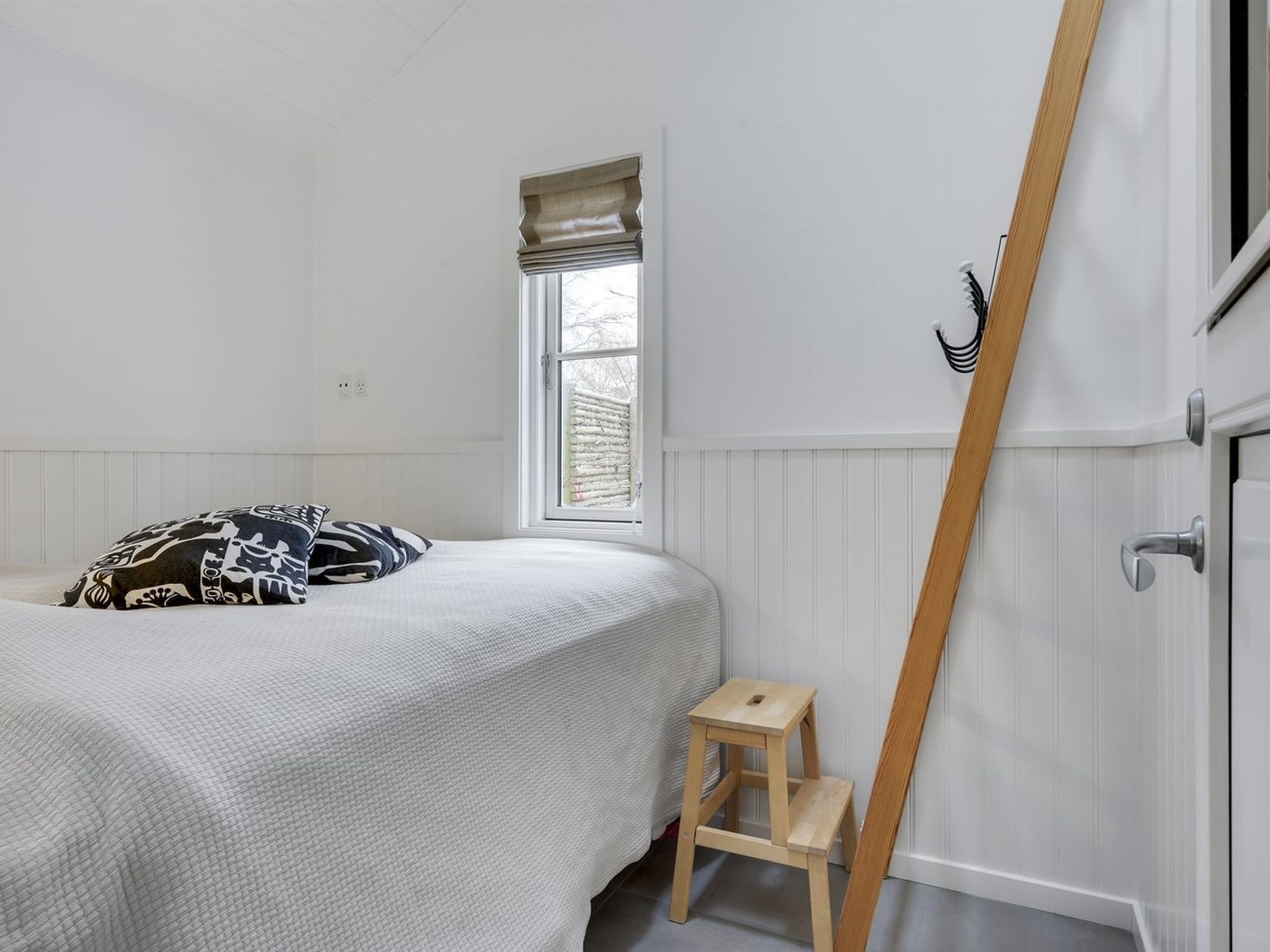 A bedroom with a bed, a window, a wooden ladder, and a door.