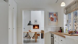 A modern kitchen with white cabinetry, a central island, a built-in fireplace, and a dining area with chairs. - "Emely" - 700m from the sea by Interhome (Jægerspris)