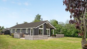 Une maison moderne dotée d’une grande terrasse, d’un espace barbecue et d’un foyer extérieur dans le jardin.