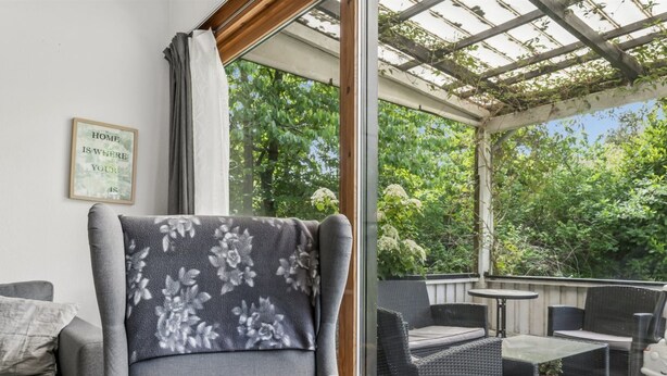 A covered outdoor seating area with a grey armchair, wicker furniture, and a framed quote on the wall. - "Gadde" - 1km from the sea by Interhome (Hundested)