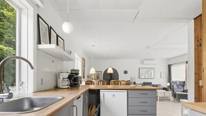 A modern kitchen with a built-in dishwasher, a coffee machine, and a dining area with wooden chairs. - "Gadde" - 1km from the sea by Interhome (Hundested)