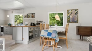 A modern kitchen with a dining area, featuring a central island, wooden chairs, and a view of greenery. - "Gadde" - 1km from the sea by Interhome (Hundested)