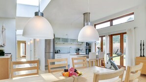 Une cuisine moderne avec un coin repas, de grandes fenêtres et une vue sur l’extérieur.