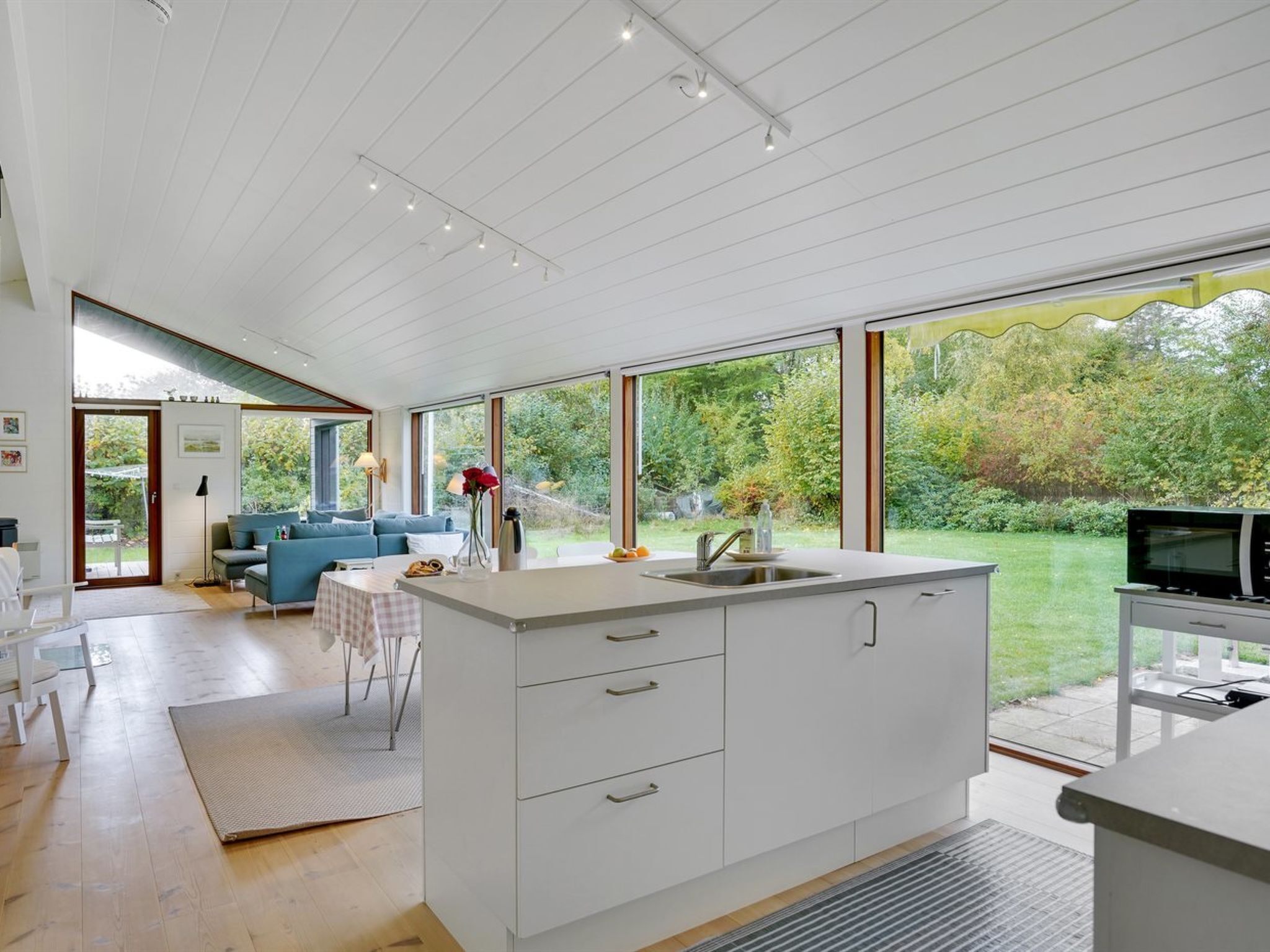 A modern kitchen with large windows, a dining area with a blue sofa, and a TV on a stand.