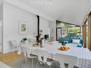 A modern living room with a sofa, a dining table with chairs, a fireplace, and a large window with a view of greenery. - "Aino" - 1km from the sea by Interhome (Liseleje)