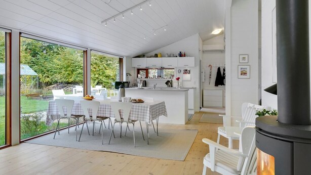 Eine moderne Küche mit weißen Schränken, ein Essbereich mit Tisch und Stühlen sowie ein großes Fenster mit Blick auf einen Garten.