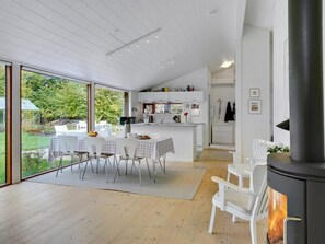 Een moderne keuken met witte kastjes, een eethoek met tafel en stoelen, en een groot raam met uitzicht op een tuin.