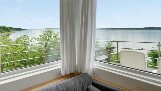 A room with a view of a lake, a white curtain, a bench, and a chair. - "Grumme" - 30m to the fjord by Interhome (Ølsted)