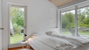 Une chambre à coucher moderne avec un grand lit, une petite table de chevet et une vue sur l’extérieur.