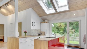 Une cuisine moderne dotée d’un îlot central, d’un coin repas et d’une grande porte-fenêtre coulissante donnant sur un jardin.
