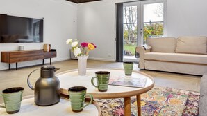 A modern living room with a flat-screen TV, a sofa, a coffee table with mugs and a kettle, and a vase with flowers. - "Ribanna" - 650m from the sea by Interhome (Gilleleje)