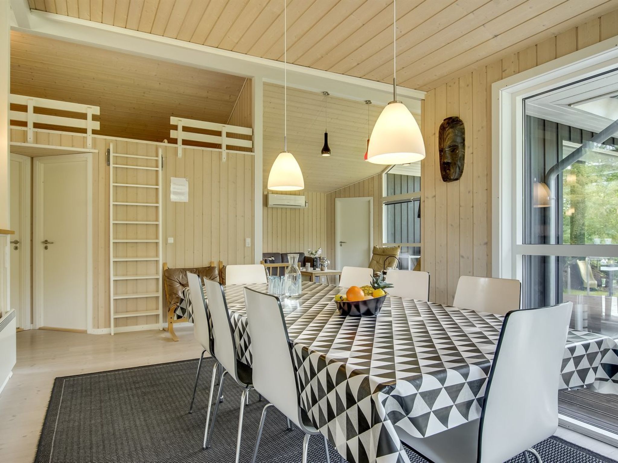 Un coin repas avec une nappe à carreaux, des chaises blanches et des luminaires suspendus.