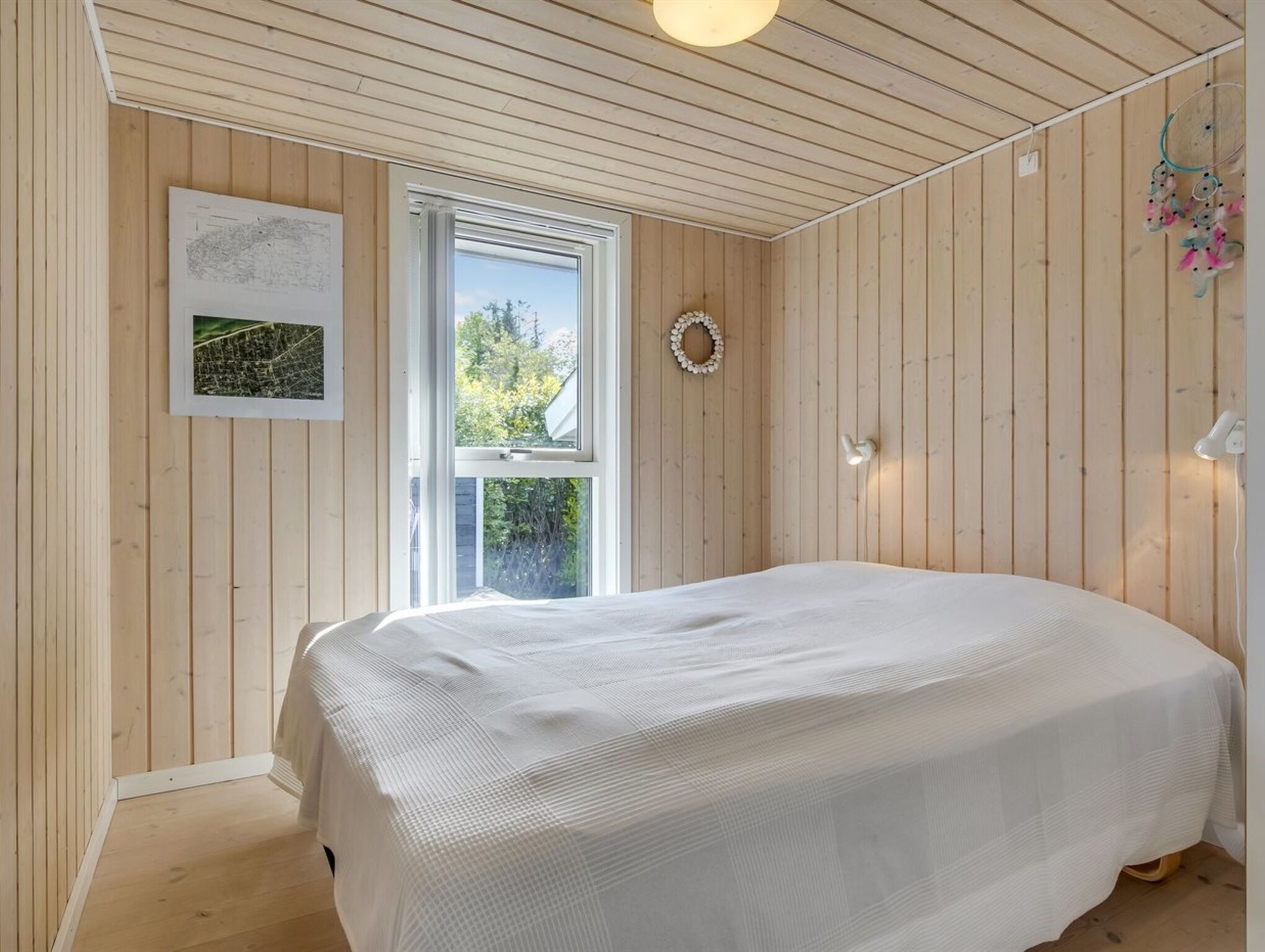 Ein Schlafzimmer mit einem großen Bett, Holzwänden, einem Fenster und einer Wandleuchte.