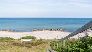 Ein Strand mit einer Holztreppe, die zum Ufer führt, umgeben von viel Grün.